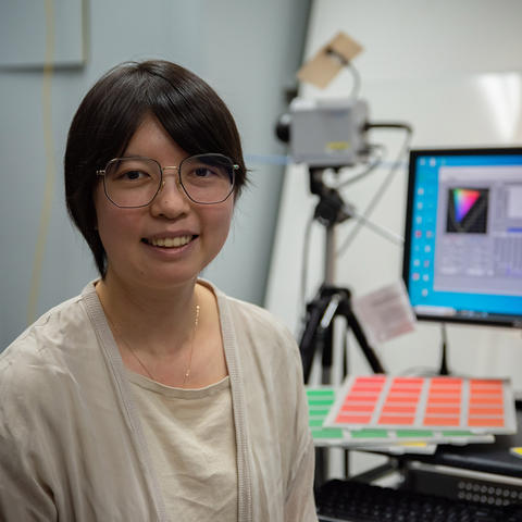 Jane Li poses at her desk with color samples in the background.